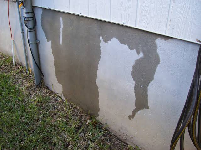 Damp and discolored exterior foundation wall indicating possible moisture seepage